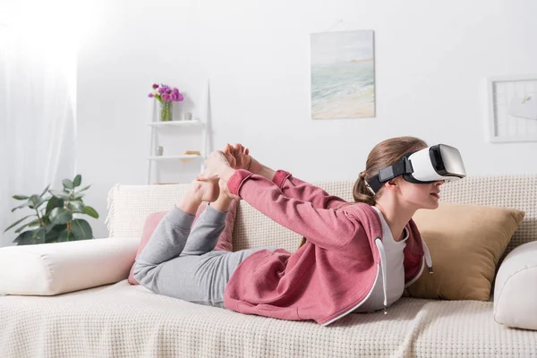 Menina alongando-se no sofá com fone de ouvido realidade virtual em casa — Fotografia de Stock