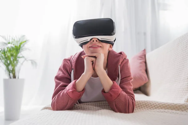 Девушка лежит на диване и смотрит что-то с гарнитурой виртуальной реальности дома — стоковое фото