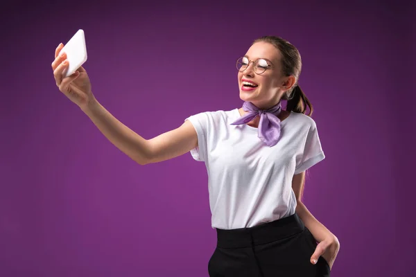 Девушка делает селфи со смартфоном, изолированным на фиолетовый — стоковое фото