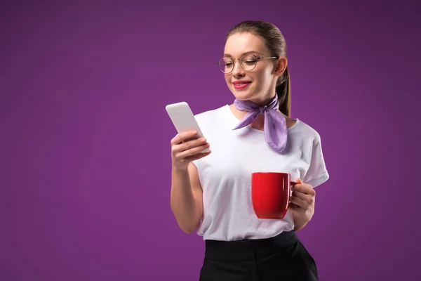 Fille avec tasse de café rouge en utilisant smartphone isolé sur violet — Photo de stock