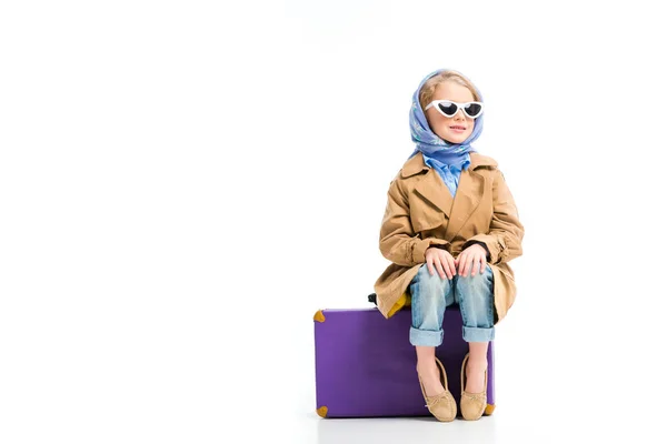 Vista de niño con estilo en pañuelo para la cabeza y gafas de sol sentado en la maleta aislado en blanco - foto de stock