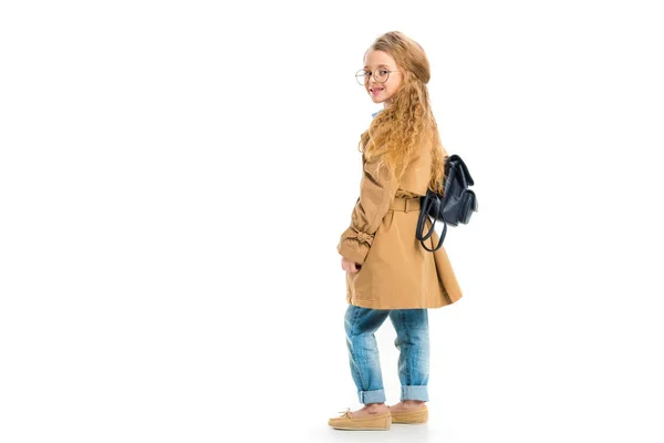 Rear view of smiling child in glasses wearing trench coat and holding bag isolated on white — Stock Photo