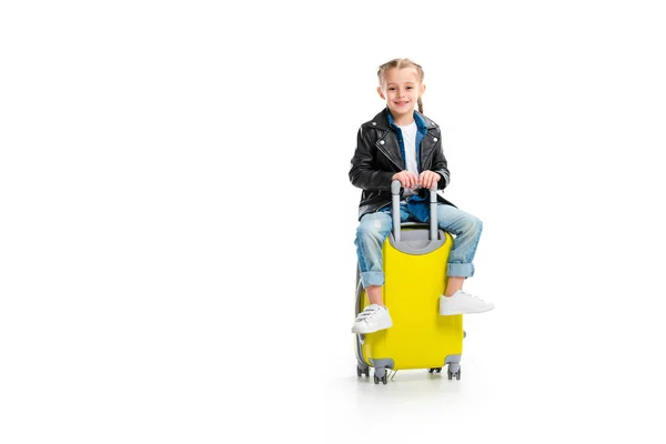 Little tourist with pigtails wearing leather jacket and sitting on wheel suitcase isolated on white — Stock Photo