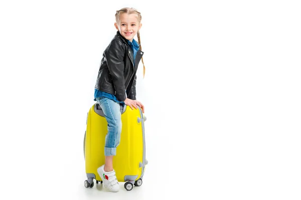 Pequeño turista sonriente sentado en la maleta de la rueda amarilla aislado en blanco - foto de stock