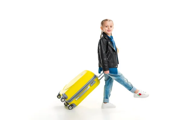 Vista lateral de la pequeña turista con coletas que transporta su maleta de rueda amarilla aislada en blanco - foto de stock