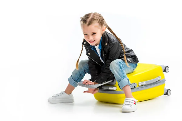 Child with pigtails sitting on lying wheel suitcase isolated on white — Stock Photo