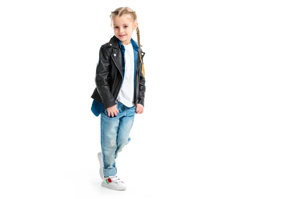 Little stylish kid wearing black leather jacket standing with fingers in pockets isolated on white — Stock Photo