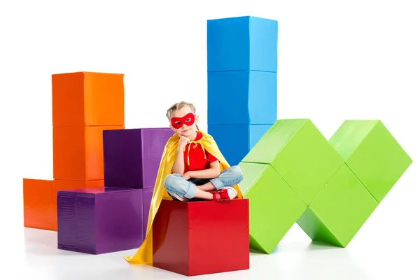 Supergirl wearing yellow cape and red mask for eyes sitting on cube isolated on white — Stock Photo