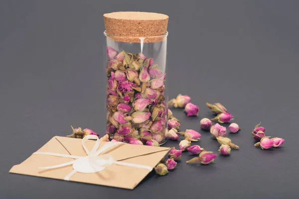 Dry pink rose buds in glass jar and envelope on grey — Stock Photo