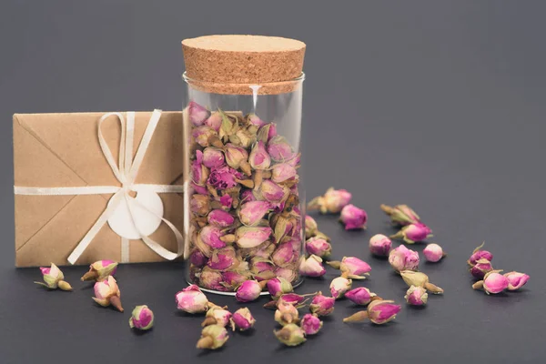Close-up view of dry rose buds in glass jar and envelope on grey — Stock Photo