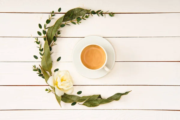 Top view of beautiful floral wreath and cup of coffee on wooden tabletop — Stock Photo