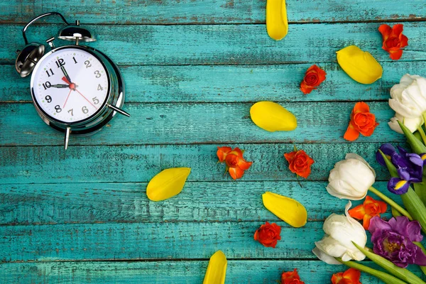 Top view of beautiful spring flowers with petals and alarm clock on turquoise wooden surface — Stock Photo