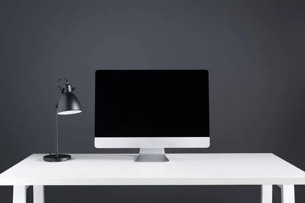 Computador de mesa moderno com tela em branco e lâmpada na mesa no espaço de trabalho — Fotografia de Stock
