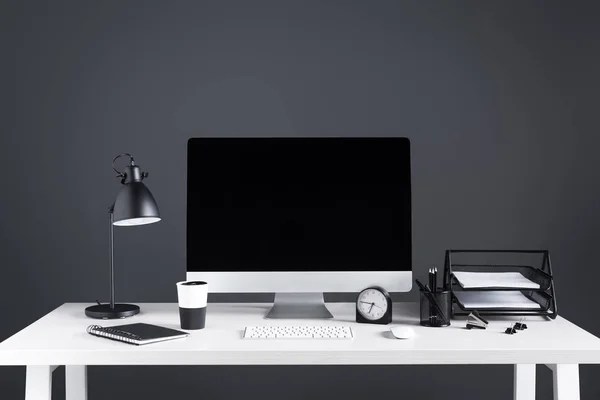 Computadora de escritorio con pantalla en blanco, reloj y suministros de oficina en el lugar de trabajo - foto de stock