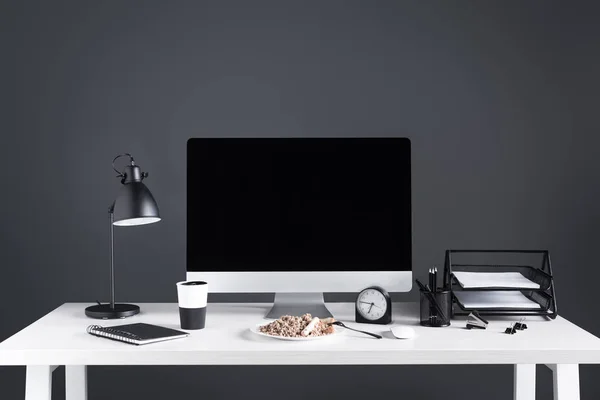 Ordinateur de bureau avec écran vierge, nourriture sur plaque et fournitures de bureau sur le lieu de travail — Photo de stock