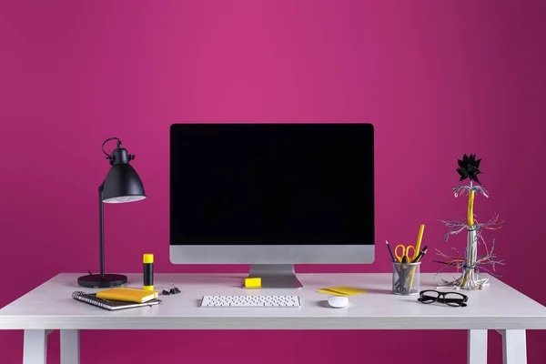 Computador desktop com tela em branco, lâmpada e vários materiais de escritório na mesa no local de trabalho — Fotografia de Stock