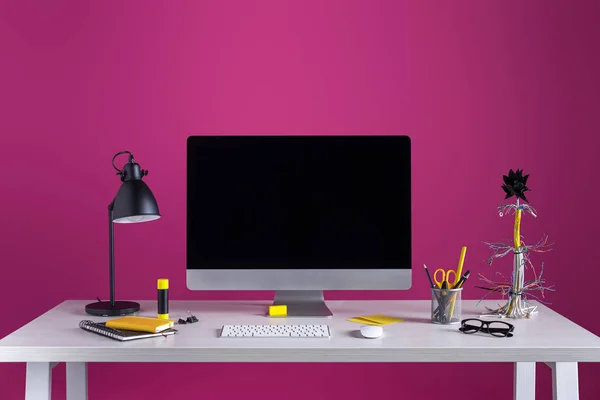 Computadora de escritorio con pantalla en blanco, lámpara y varios suministros de oficina en la mesa en el lugar de trabajo - foto de stock