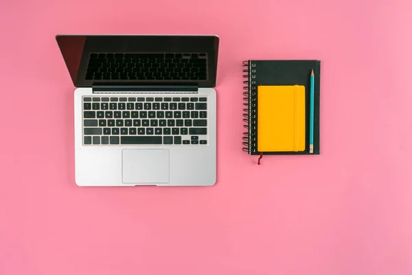 Draufsicht auf Laptop mit leerem Bildschirm und Notizbücher mit Bleistift auf rosa — Stockfoto