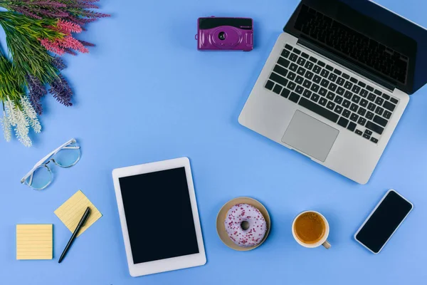 Vista superior de dispositivos digitales, flores, taza de café con donut y cámara en azul - foto de stock