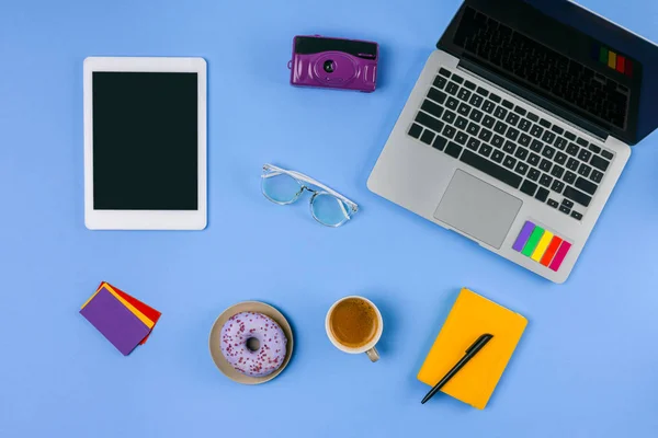 Vista superior do laptop, tablet digital, xícara de café com donut e câmera em azul — Fotografia de Stock