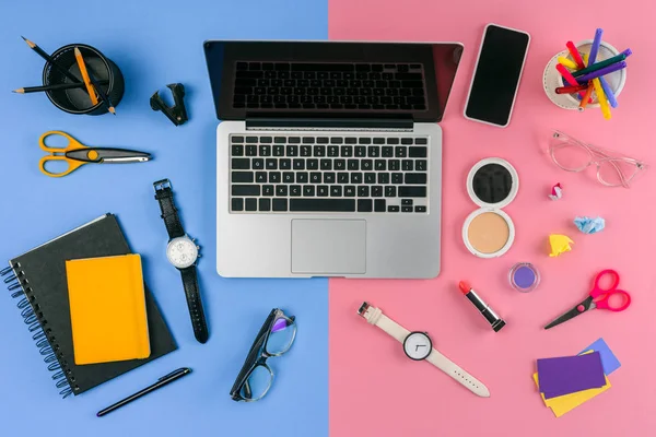 Top view of laptop, smartphone and cosmetics with office supplies divided at male and female workplace — Stock Photo