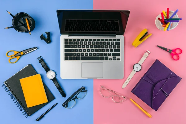 Top view of laptop with blank screen, eyeglasses, wristwatches and notebooks divided at male and female workplace — Stock Photo