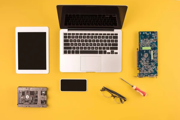 Draufsicht auf digitale Geräte mit schwarzen Bildschirmen und Motherboard und Hardware auf gelb — Stockfoto