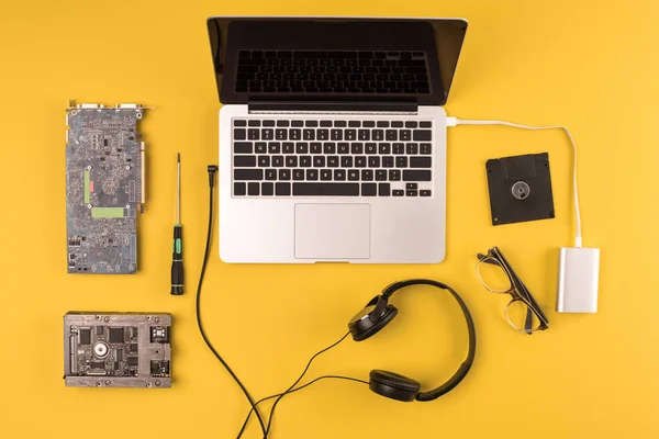 Vista superior de laptop com fones de ouvido, óculos e ferramentas em amarelo — Fotografia de Stock
