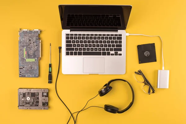 Vista superior del portátil con auriculares, anteojos y herramientas en amarillo - foto de stock