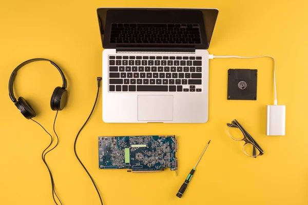 Top view of laptop with headphones, eyeglasses and motherboard on yellow — Stock Photo