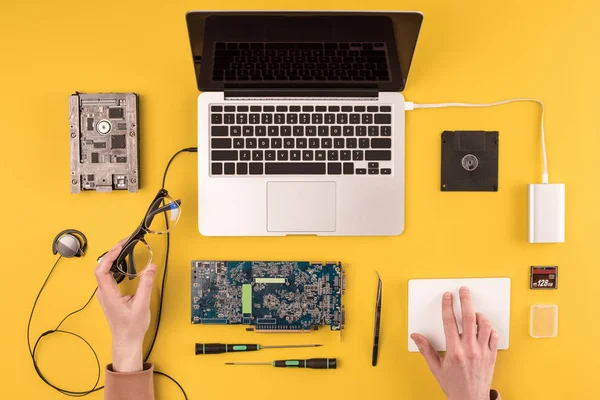 Partial top view of person holding eyeglasses and fixing laptop on yellow — Stock Photo