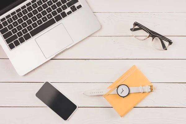 Vue de dessus de l'ordinateur portable, smartphone, montre-bracelet et lunettes sur le dessus de table en bois — Photo de stock