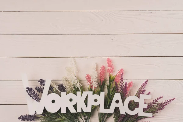 Top view of beautiful blooming flowers and word workplace on wooden surface — Stock Photo