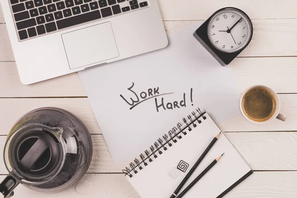 Vue du haut de l'ordinateur portable, horloge, café et inscription travailler dur dans le carnet — Photo de stock