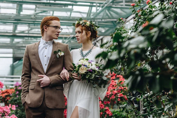 Schöne stylische junge Braut und Bräutigam gehen zusammen im botanischen Garten — Stockfoto