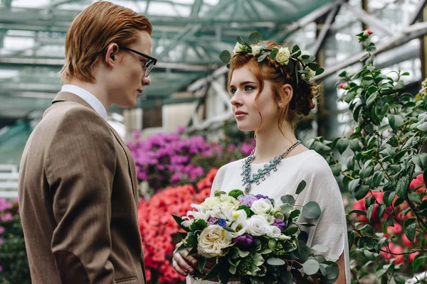 Elegante joven novio y hermosa novia pelirroja mirándose en el jardín botánico - foto de stock