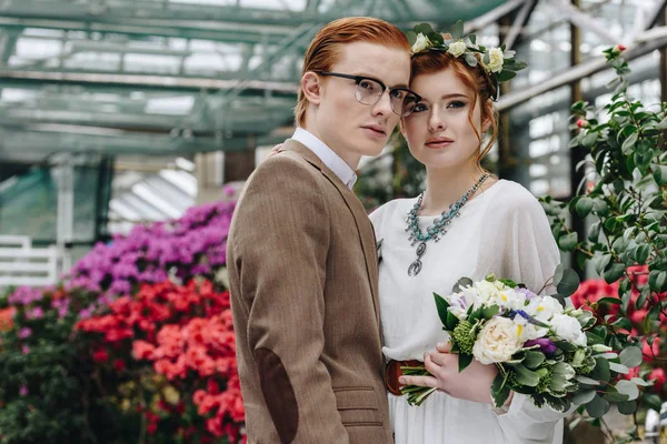 Beau élégant jeune couple de mariage rousse debout avec bouquet et détournant les yeux — Photo de stock