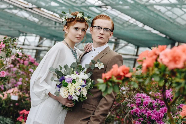 Belo elegante jovem casal de cabelos ruivos de pé juntos entre flores no jardim botânico — Fotografia de Stock