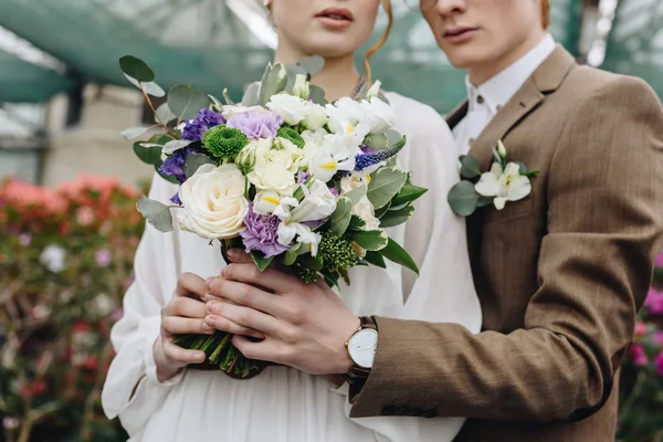 Recortado tiro de elegante pareja joven celebración de hermoso ramo de bodas - foto de stock