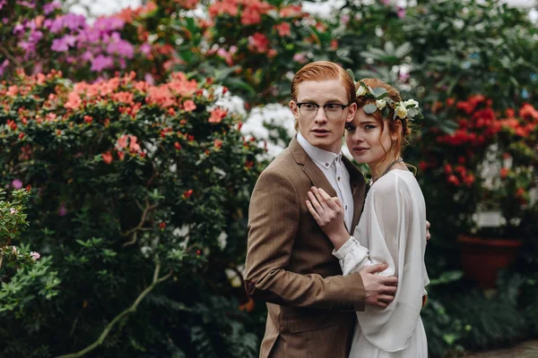 Красивая молодая элегантная свадебная пара, стоящая вместе между цветами — стоковое фото