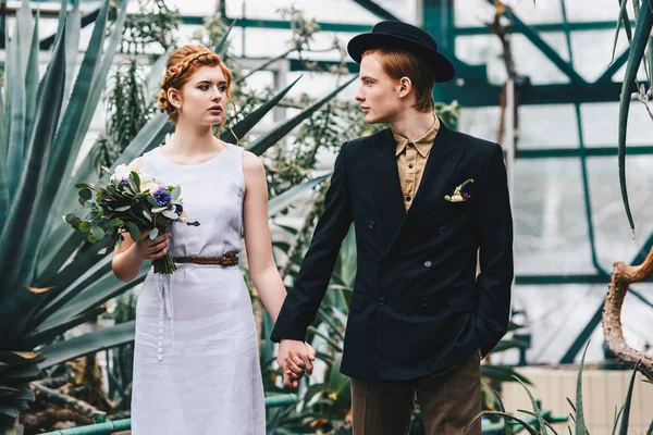 Красива молода весільна пара тримає руки і дивиться один на одного в ботанічному саду — стокове фото