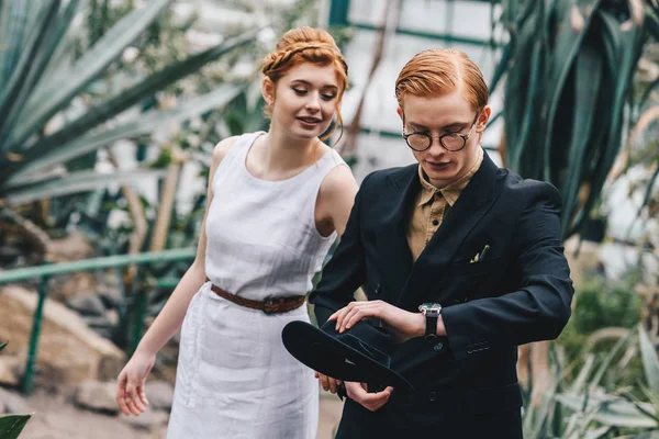Schönes junges rothaariges Hochzeitspaar schaut auf Armbanduhr im botanischen Garten — Stockfoto