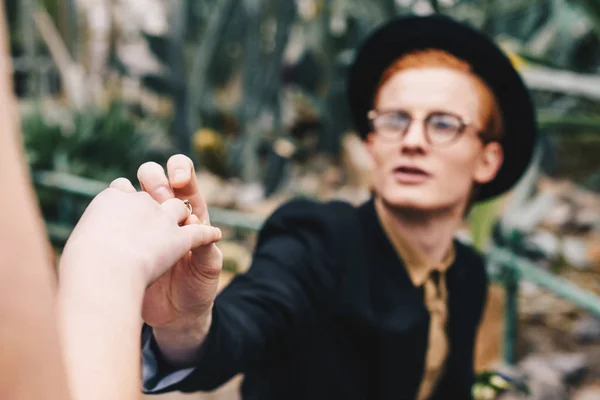 Recortado disparo de hombre joven con estilo en sombrero y gafas haciendo propuesta y poniendo anillo a la chica - foto de stock