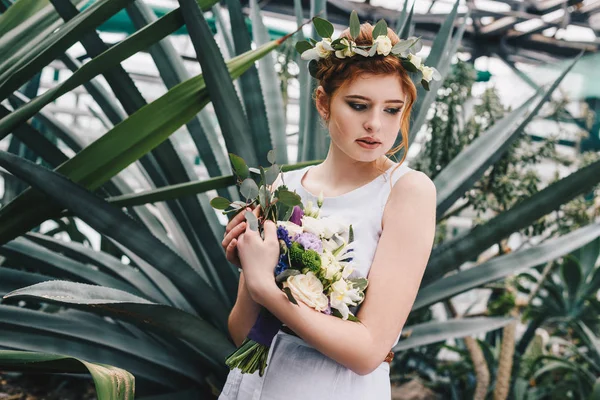 Beautiful tender young redhead bride holding wedding bouquet in botanical garden — Stock Photo