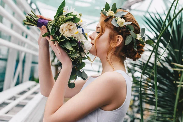 Side view of beautiful young bride in floral wreath holding wedding bouquet — Stock Photo