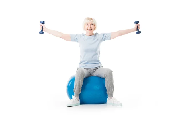 Senior sportswoman with dumbbells in wide hands sitting on fitness ball isolated on white — Stock Photo
