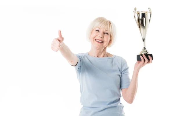 Retrato de deportista senior sonriente mostrando un gesto de pulgar hacia arriba y sosteniendo trofeo aislado en blanco - foto de stock