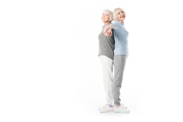 Lächelnde Seniorinnen, die Rücken an Rücken isoliert auf weiß stehen — Stockfoto