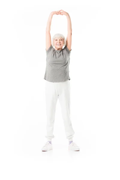 Улыбающаяся старшая спортсменка с поднятыми руками делает упражнения изолированные на белом — стоковое фото