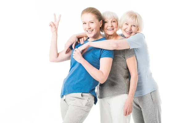 Mature sportswoman showing peace gesture while two senior sportswomen embracing her isolated on white — Stock Photo